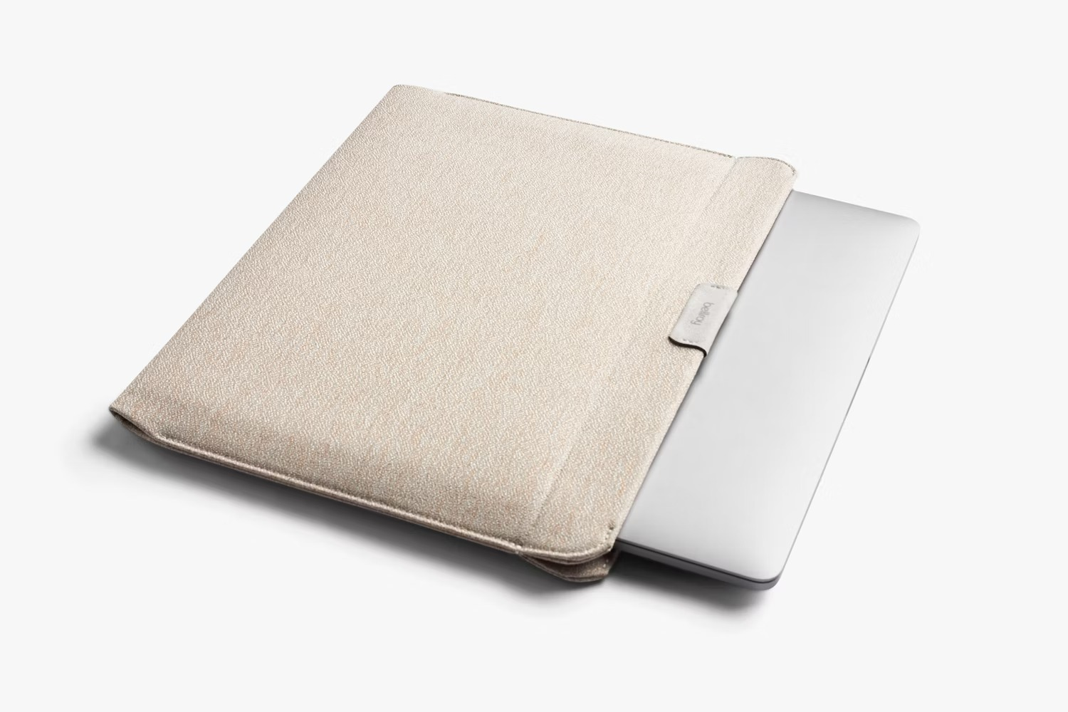 Beżowy pokrowiec z materiału mieści srebrny laptop na gładkim białym tle.