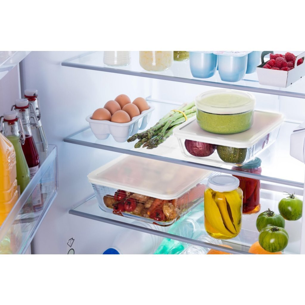 Un interno di frigorifero organizzato pieno di prodotti freschi, uova e contenitori di vetro con cibo.