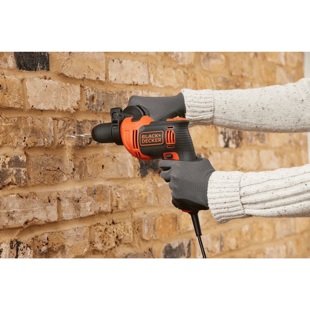 Persona perforando una pared de ladrillo con un taladro Black+Decker negro y naranja.