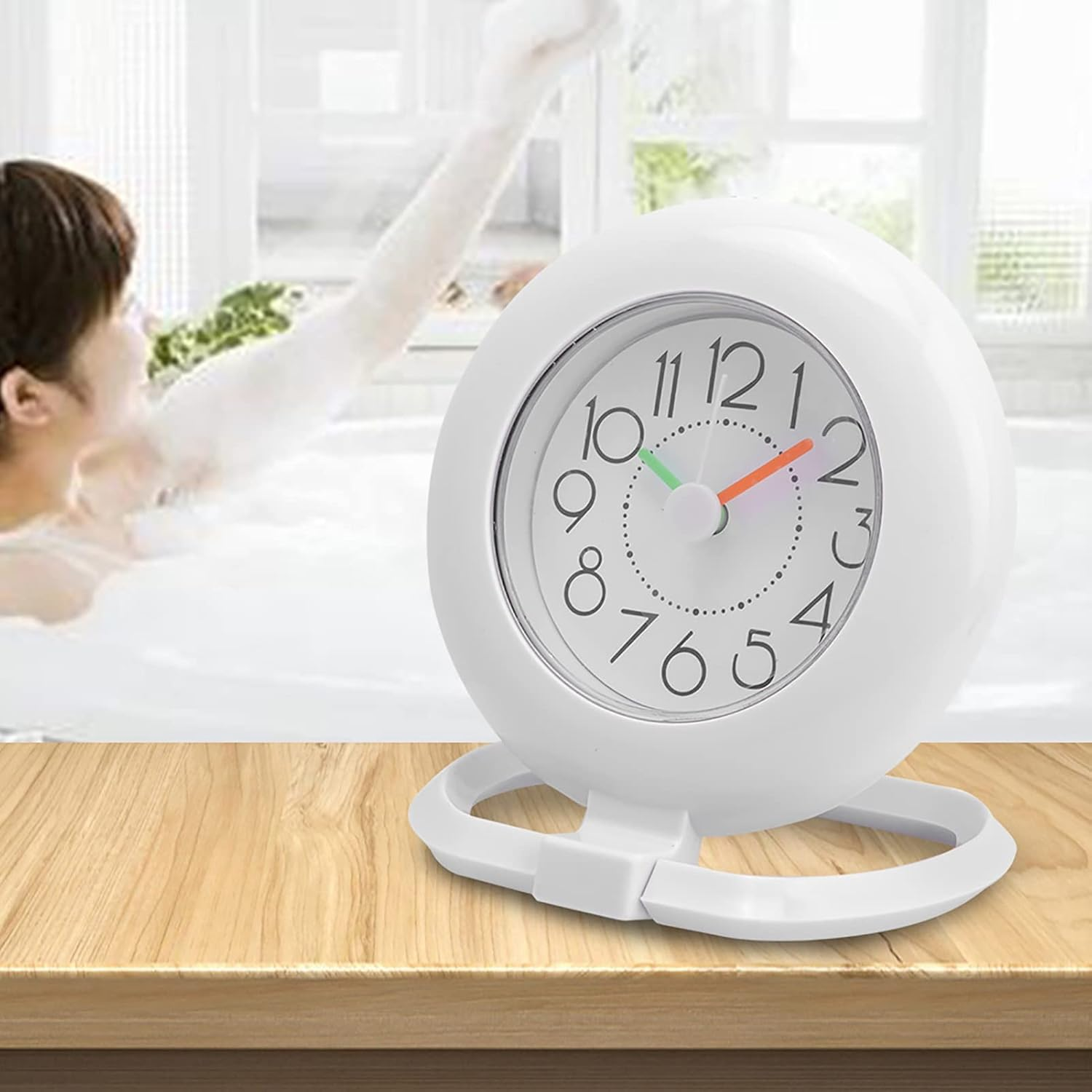 Eine weiße Uhr steht auf einer Holzoberfläche, im Hintergrund badet eine Person in Schaum.