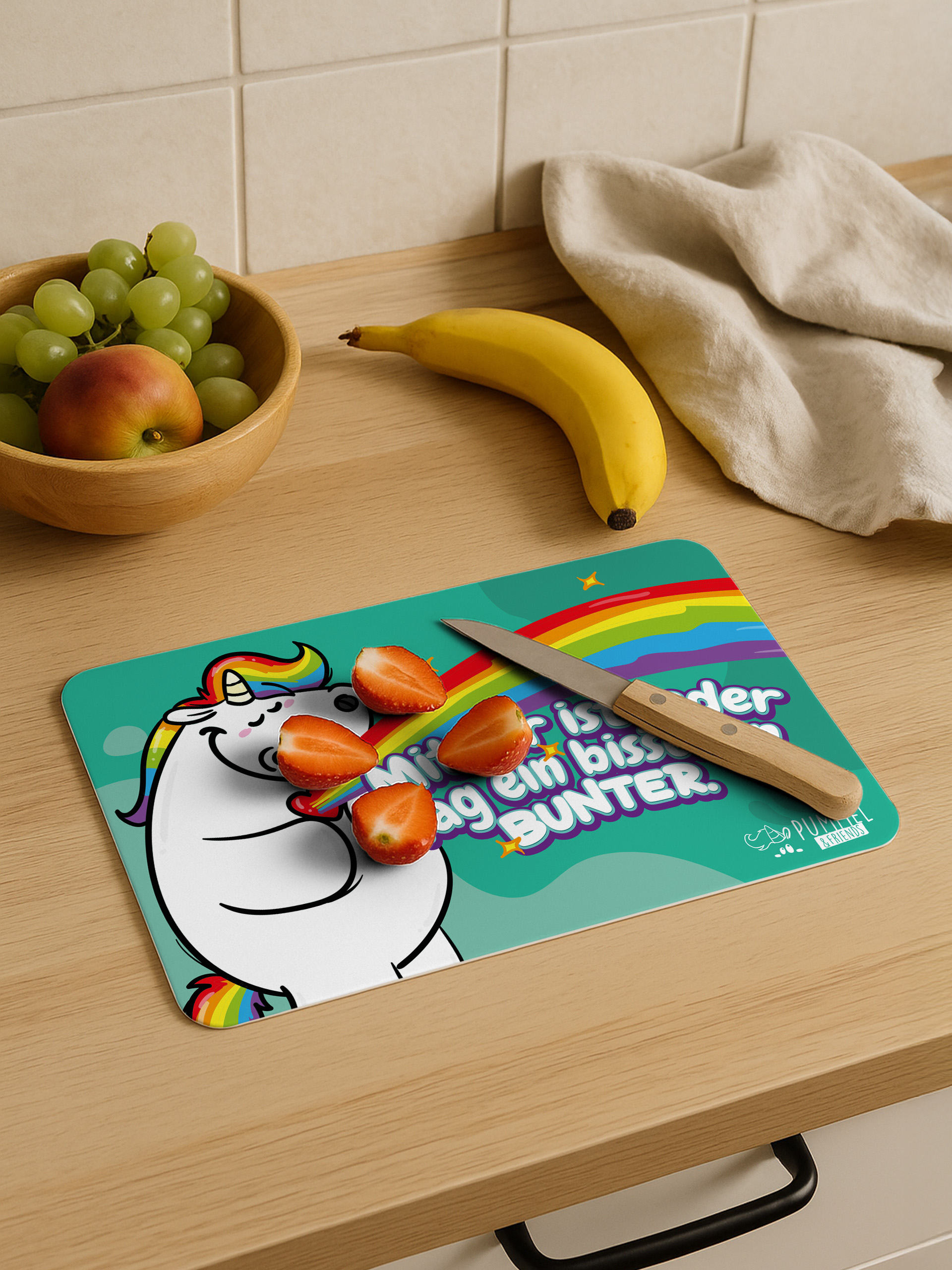 Einhorn-Schneidebrett mit Erdbeeren, Messer, Banane und Obstschale auf Holztisch.