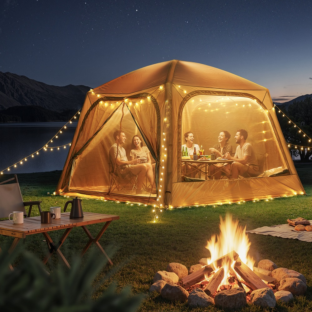 Vier Freunde lachen nachts in einem beleuchteten Zelt am Lagerfeuer und See unter sternenklarem Himmel.