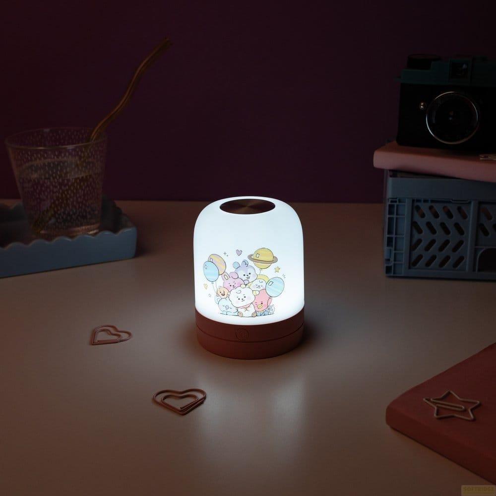 Eine leuchtende Nachttischlampe mit Zeichentrickfiguren steht auf einem Tisch neben einer Kamera und einem Glas.