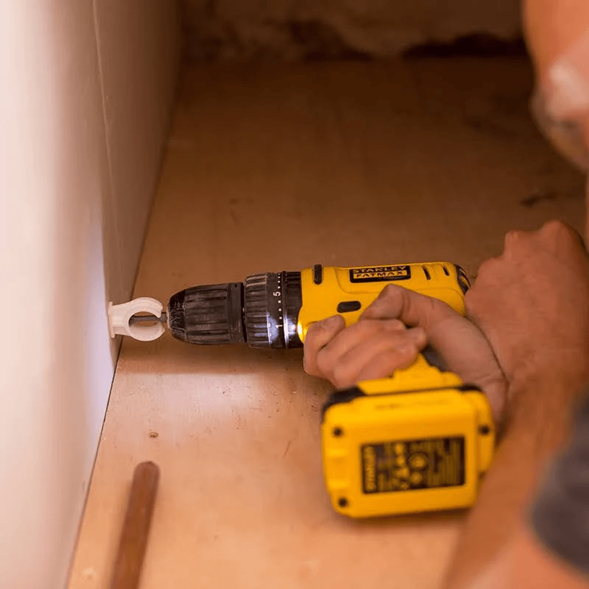Una persona usa un trapano giallo per avvitare con una clip bianca su una superficie di legno.
