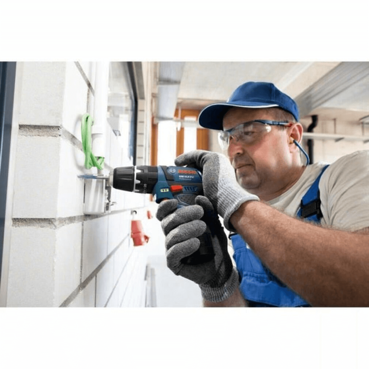 Un lavoratore con dispositivi di sicurezza usa un trapano su un muro di mattoni.