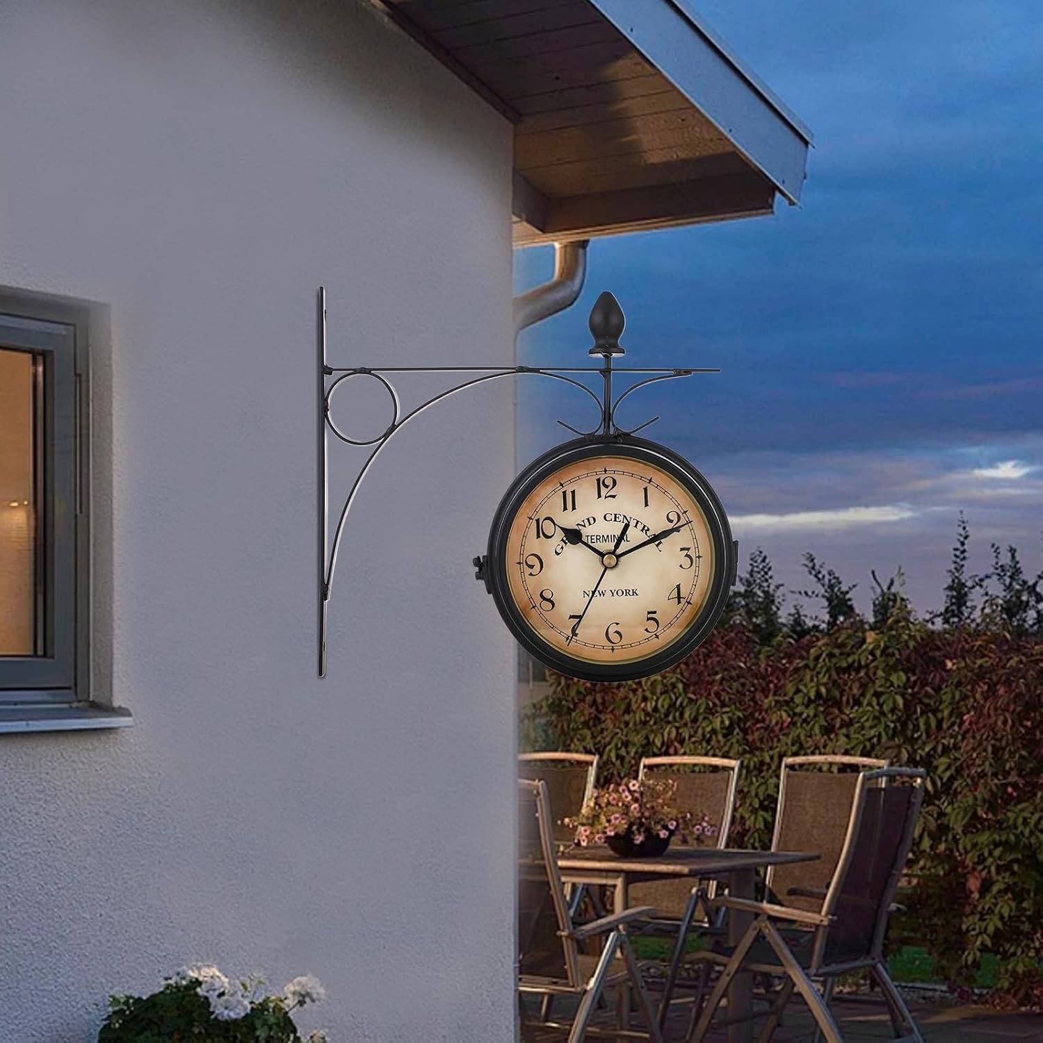 Eine Bahnhofsuhr hÃ¤ngt an einer Wand im Aussenbereich vor einer DÃ¤mmerungslandschaft.