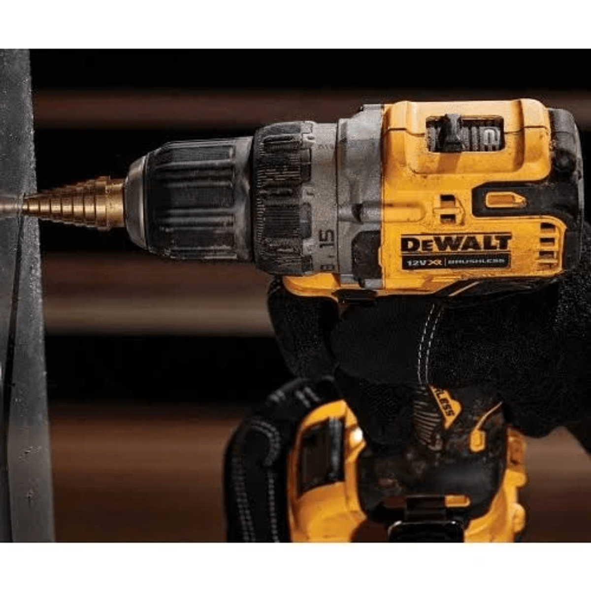 Een gehandscoekte hand houdt een geel-zwarte DeWalt boormachine vast die in metaal boort.