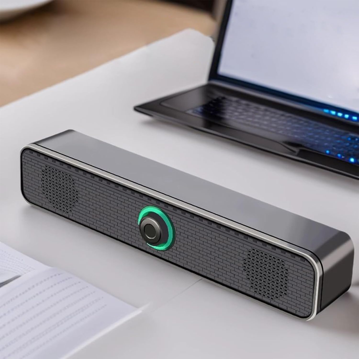Eine schwarze Soundbar mit grün leuchtendem Drehregler auf einem weißen Schreibtisch neben einem Laptop.