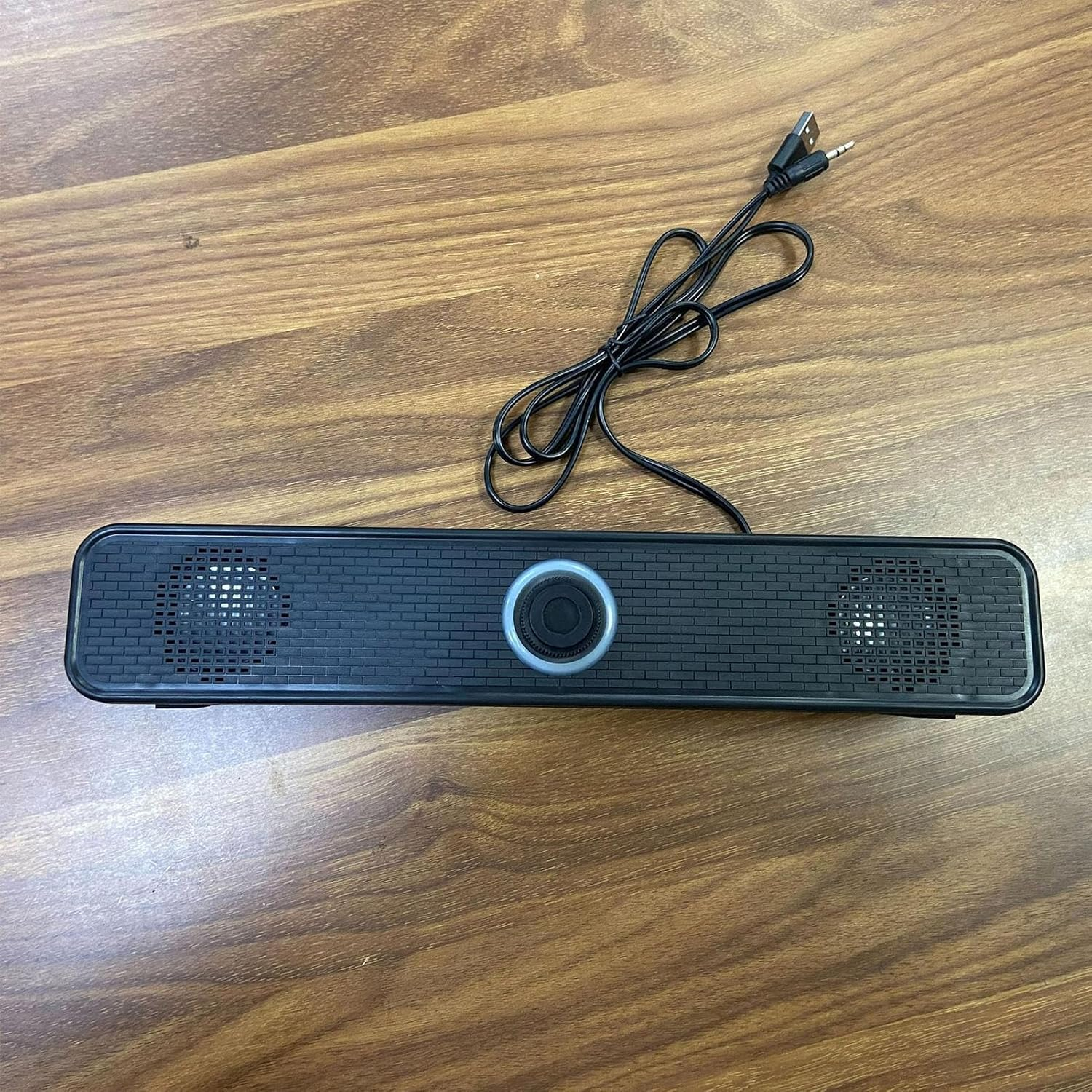 Ein langer schwarzer USB-Computerlautsprecher mit Kabel liegt auf einer Holzoberfläche.