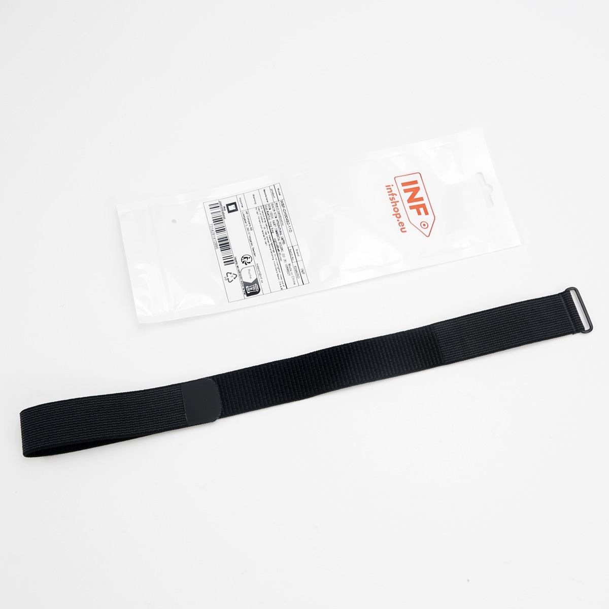 Ein langer, schwarzer Textilriemen mit Metallschnalle liegt auf weißem Grund neben einer Plastikverpackung.