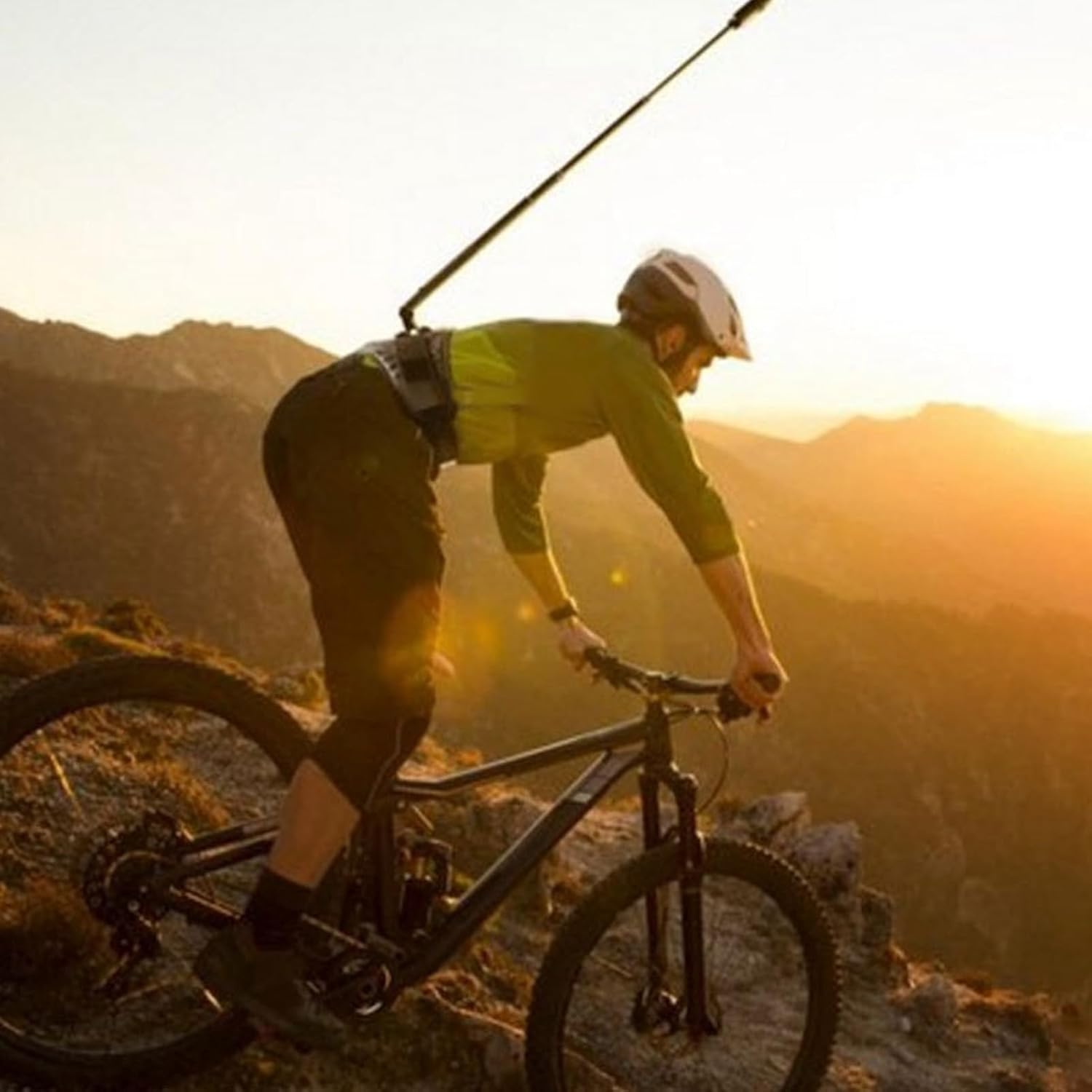 Ein Mountainbiker fährt bei Sonnenuntergang auf einem Berggrat, mit einer Kamera an einem Gürtelstab montiert.