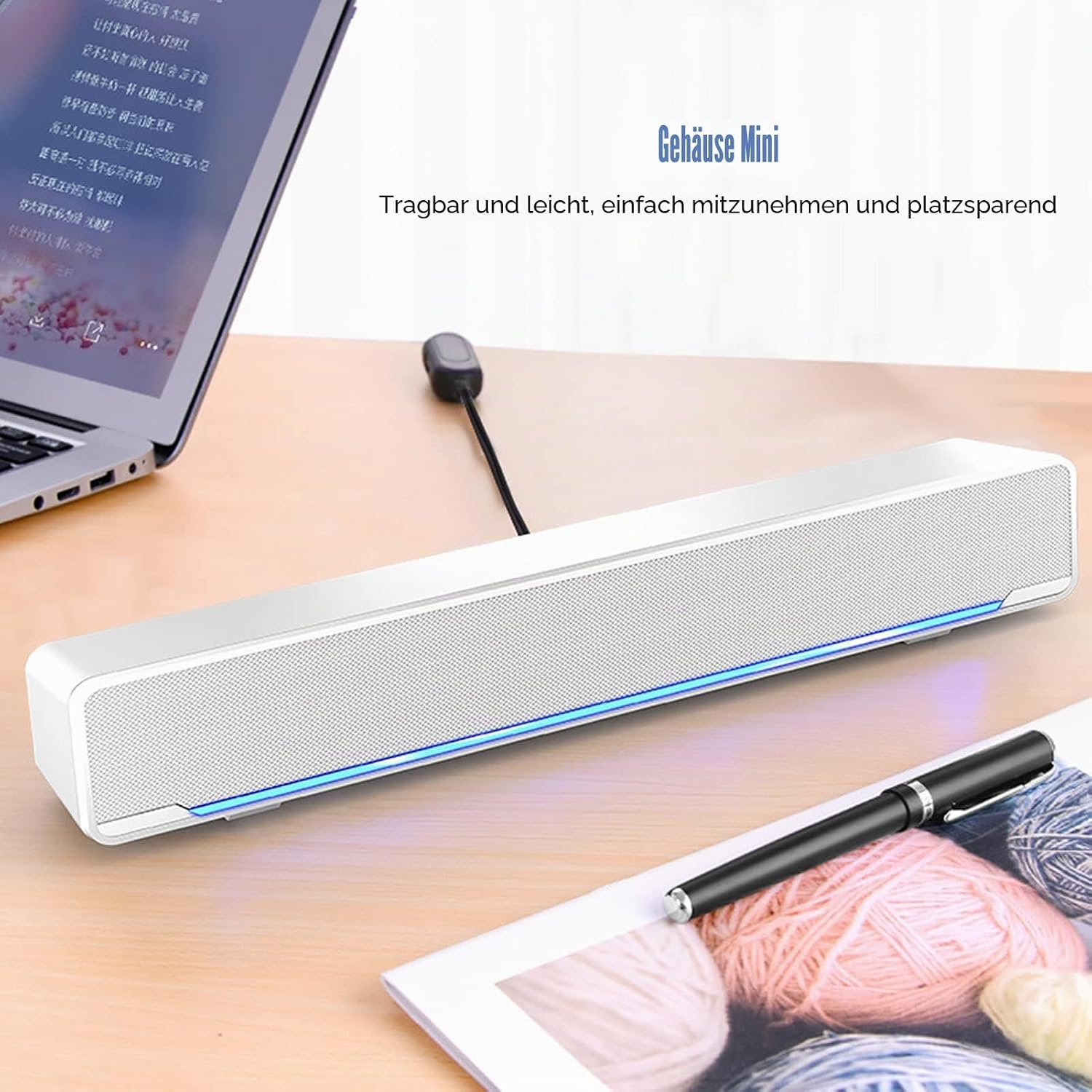 Eine weiße Mini-Soundbar mit blauer LED-Beleuchtung liegt auf einem Schreibtisch neben einem Laptop und einem Stift.