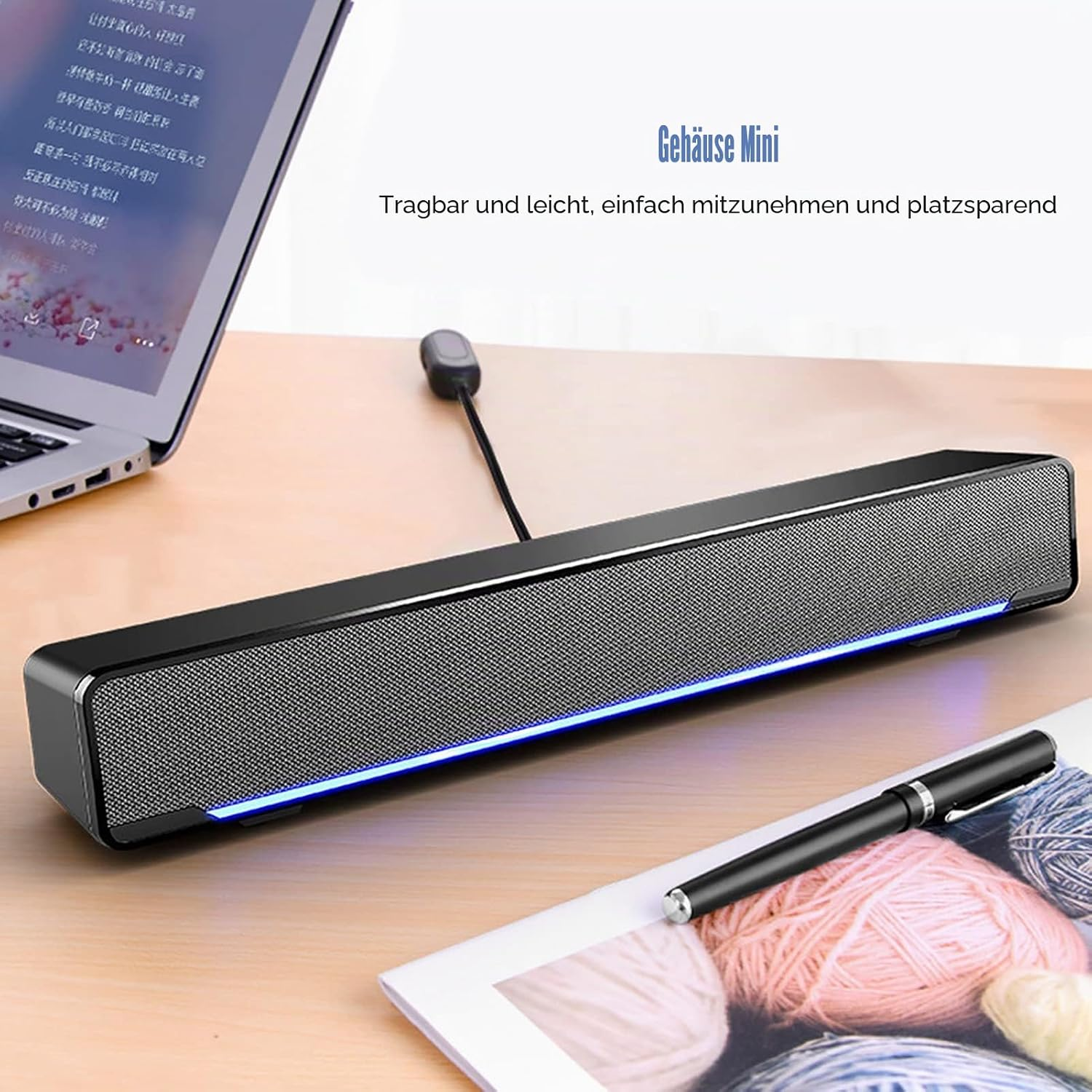 Eine lange schwarze Soundbar mit blauem Licht steht auf einem Holztisch neben einem Laptop und einem Stift.