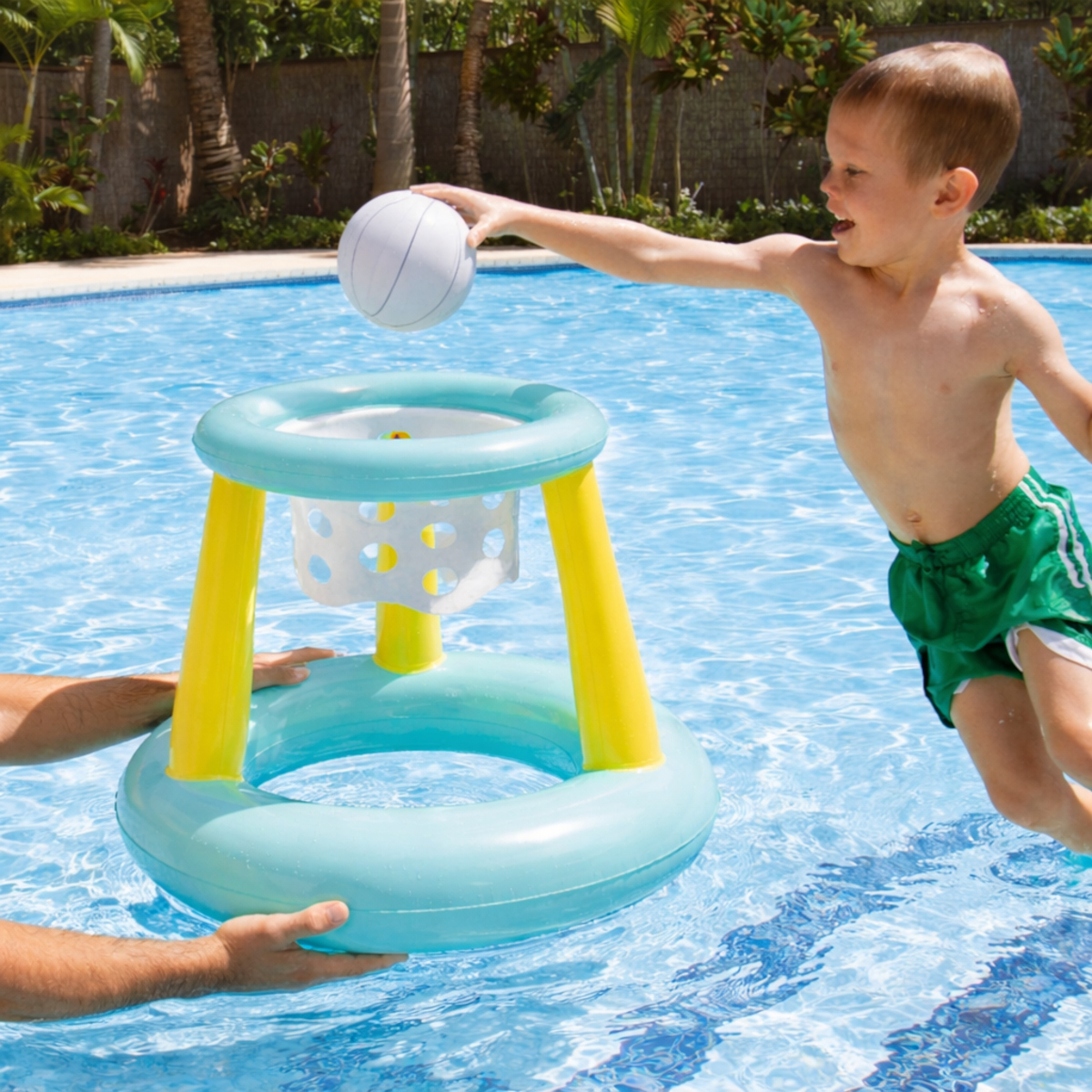 Ein Junge in grünen Shorts wirft einen Ball in einen schwimmenden Basketballkorb im Pool.