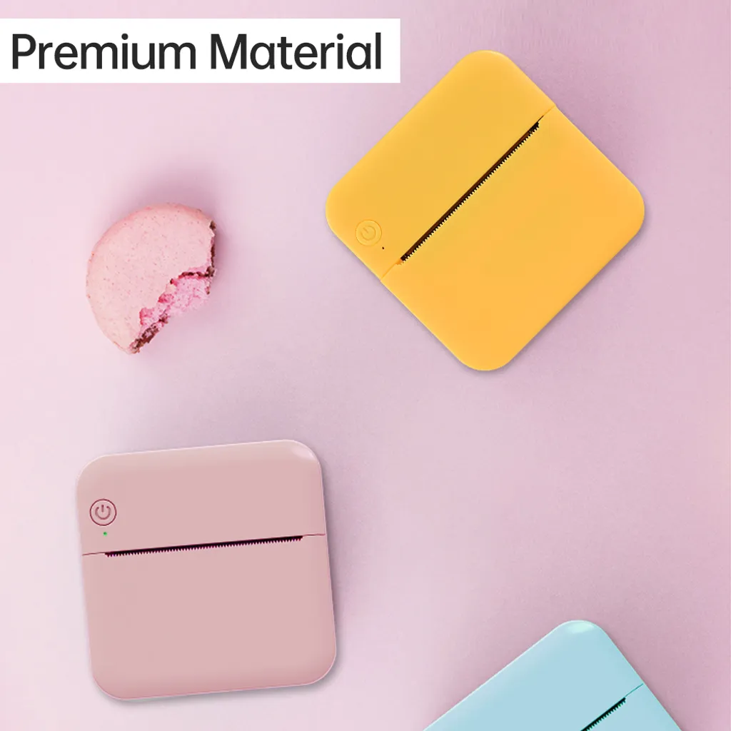 Drei bunte Mini-Drucker und ein angebissenes rosa Macaron auf rosa Hintergrund.