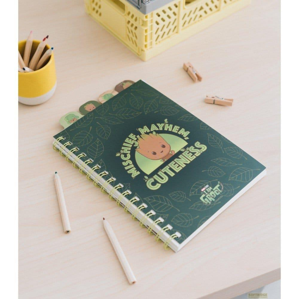 Ein grünes Notizbuch mit Groot-Illustration auf dem Einband liegt auf einem Holztisch, umgeben von Stiften.