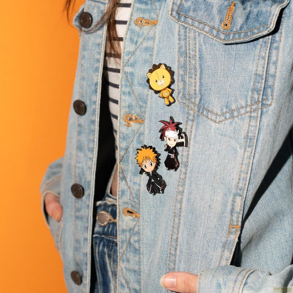 Eine Person trägt eine Jeansjacke mit drei Anime-Charakter-Emaille-Ansteckern vor orangefarbenem Hintergrund.