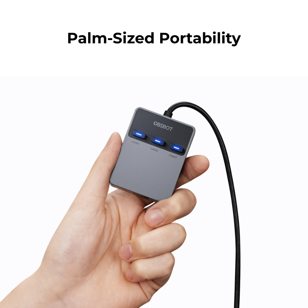 Una mano tiene un dispositivo OBSBOT grigio con tre luci blu e un cavo su sfondo bianco.