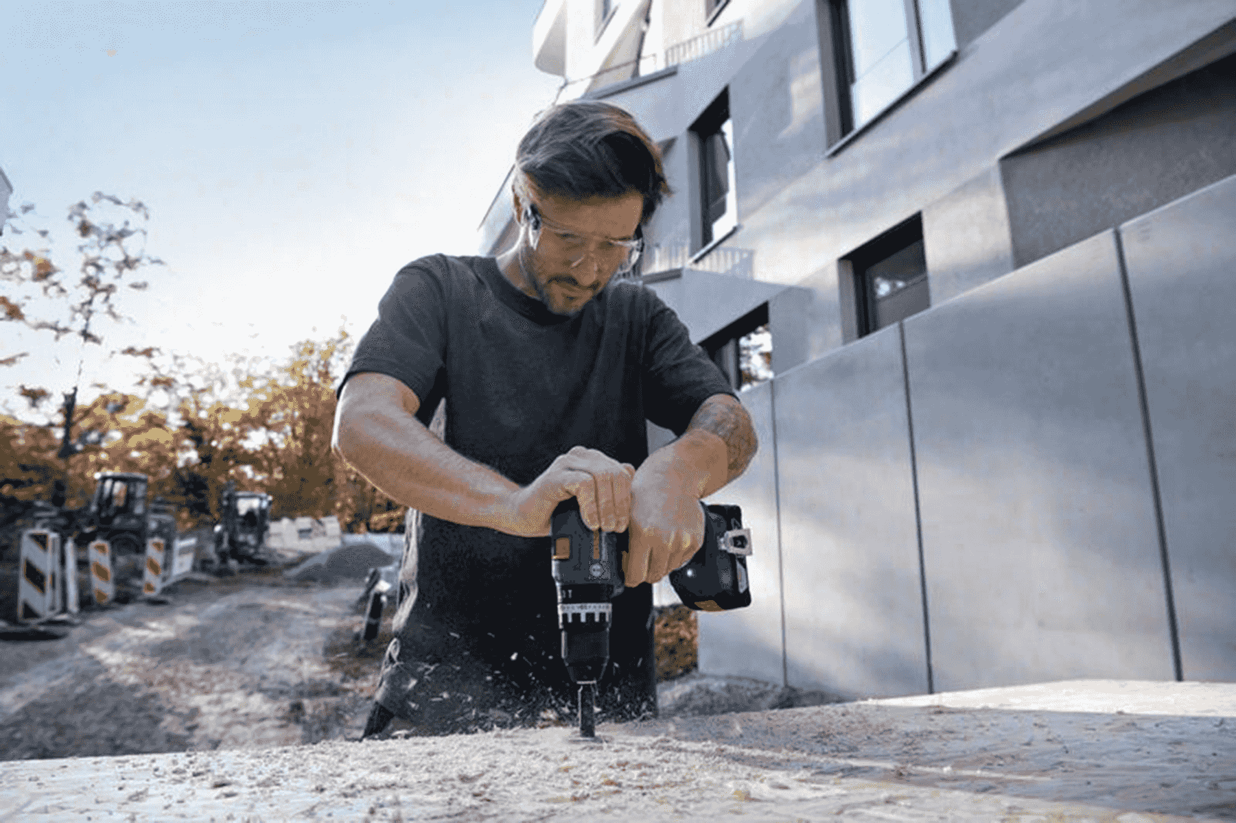 Un lavoratore usa un trapano a batteria su un pezzo di legno in un cantiere.