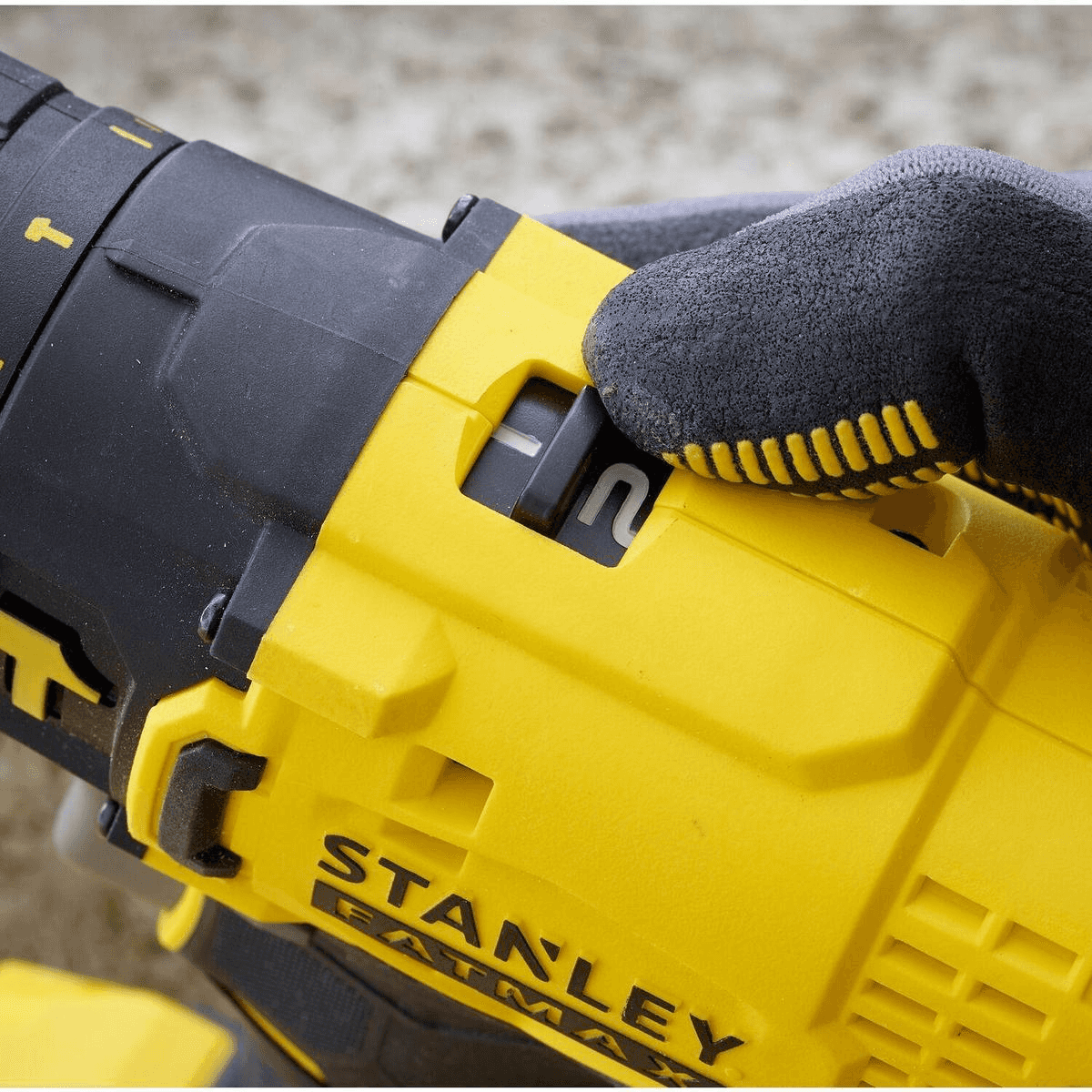 Una mano con guante ajusta el selector de velocidad en un taladro Stanley Fatmax amarillo y negro.