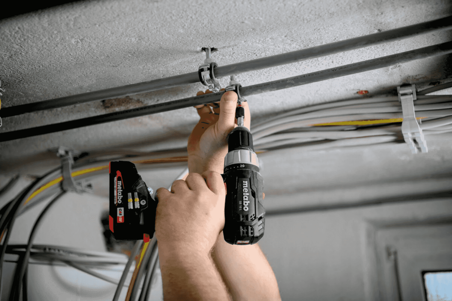 Un artigiano utilizza un trapano a batteria per montare tubi sul soffitto.