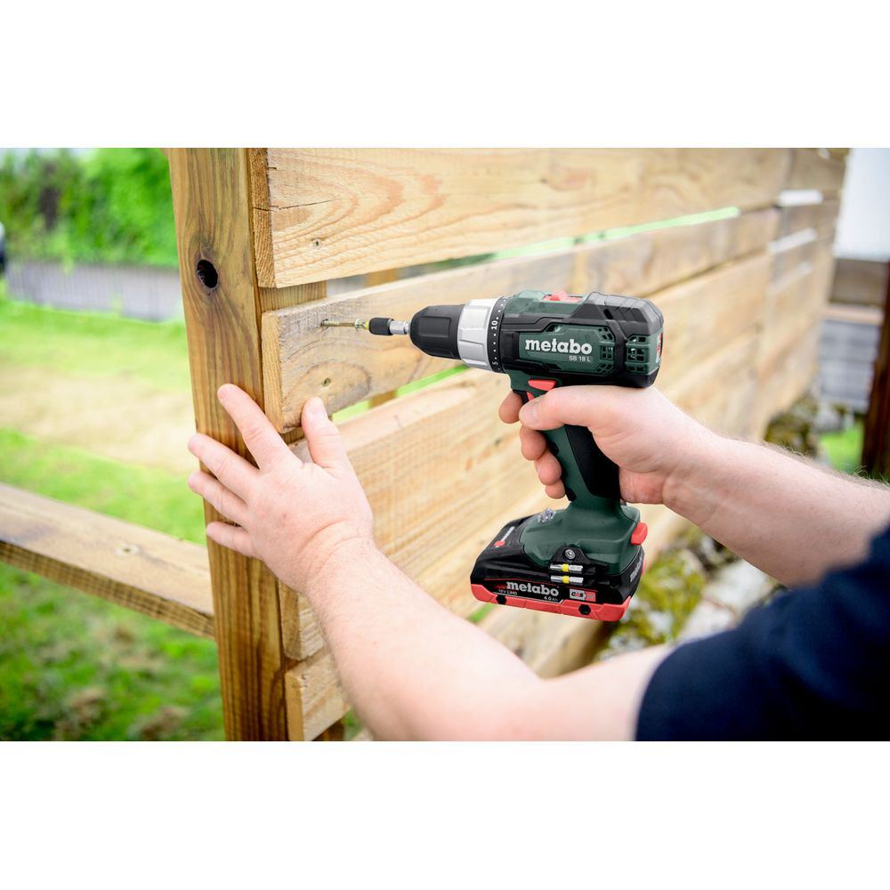 Una persona usa un taladro inalámbrico Metabo verde para atornillar una cerca de madera.