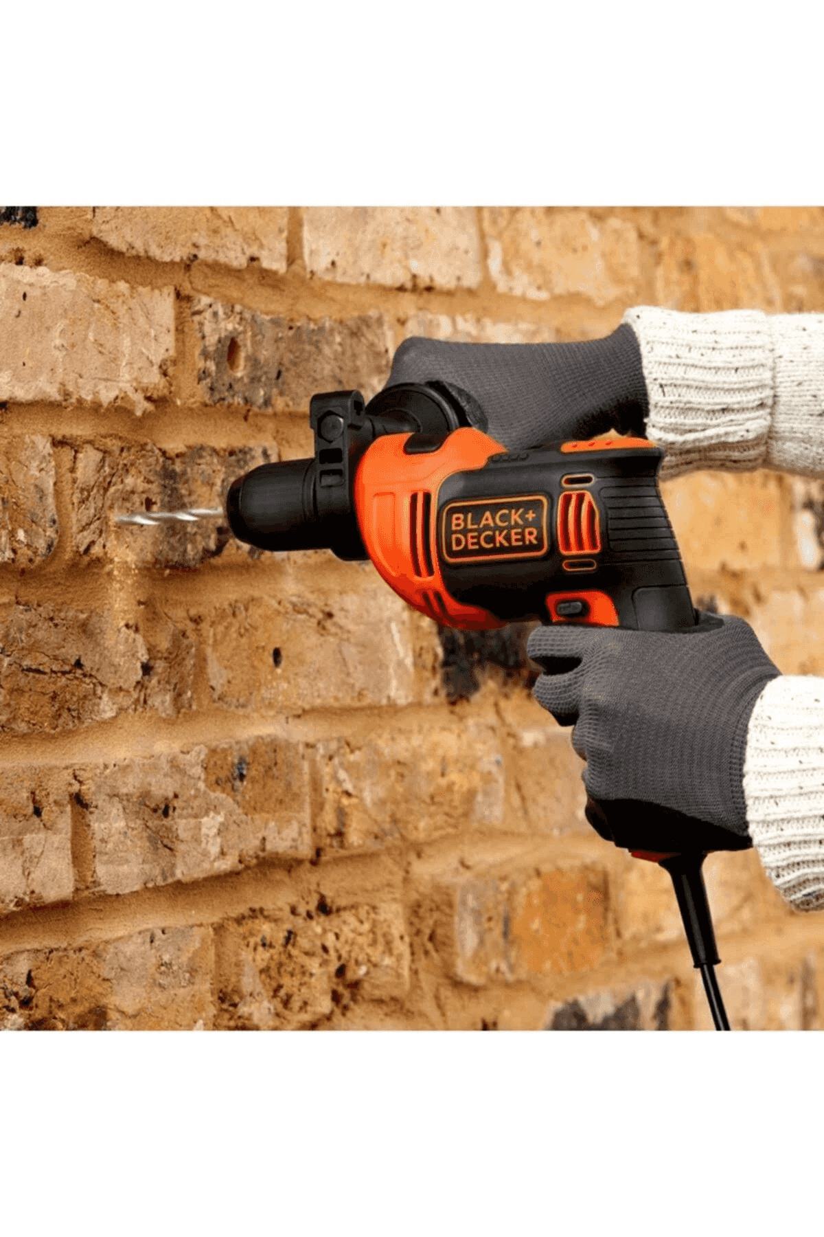 Una persona perfora una pared de ladrillo con un taladro Black+Decker naranja y negro.