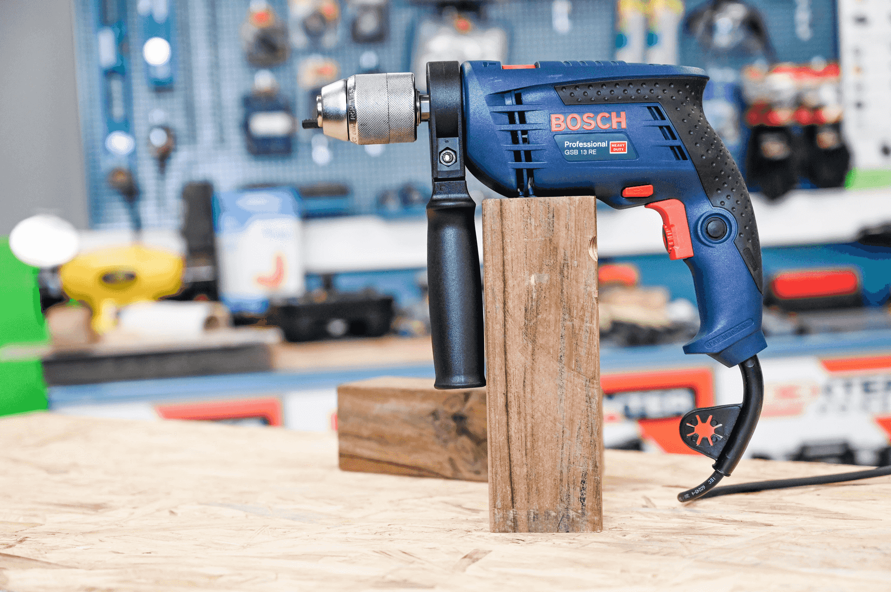 Taladro percutor Bosch azul apoyado en un bloque de madera en un taller.