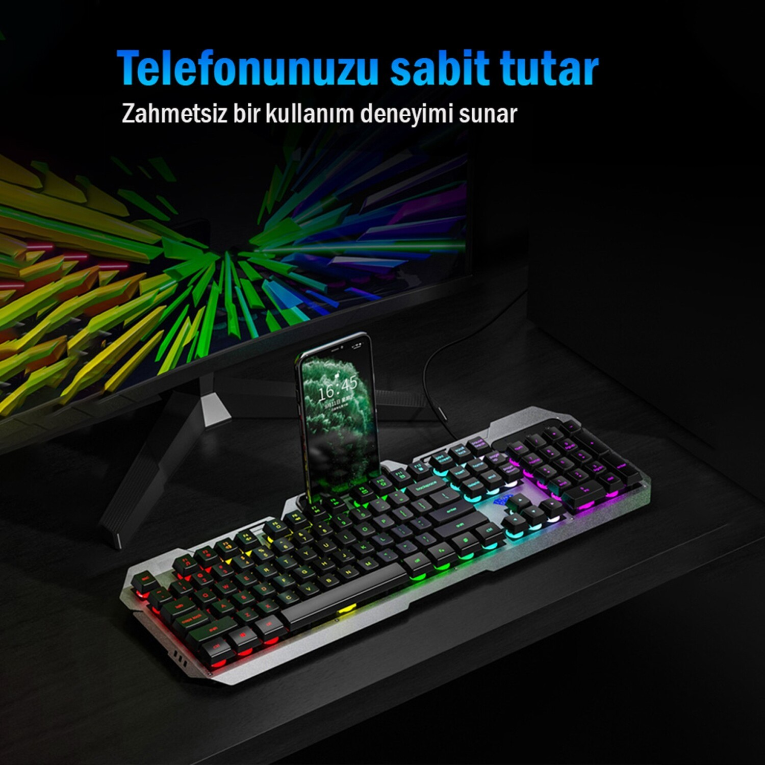Bir monitörün önünde masada duran, entegre akıllı telefon tutuculu bir RGB oyun klavyesi.
