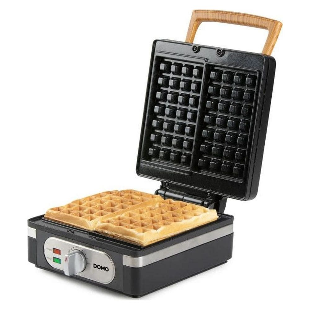 Ein schwarzes Waffeleisen mit Holzgriff und zwei frisch gebackenen, goldenen Waffeln.