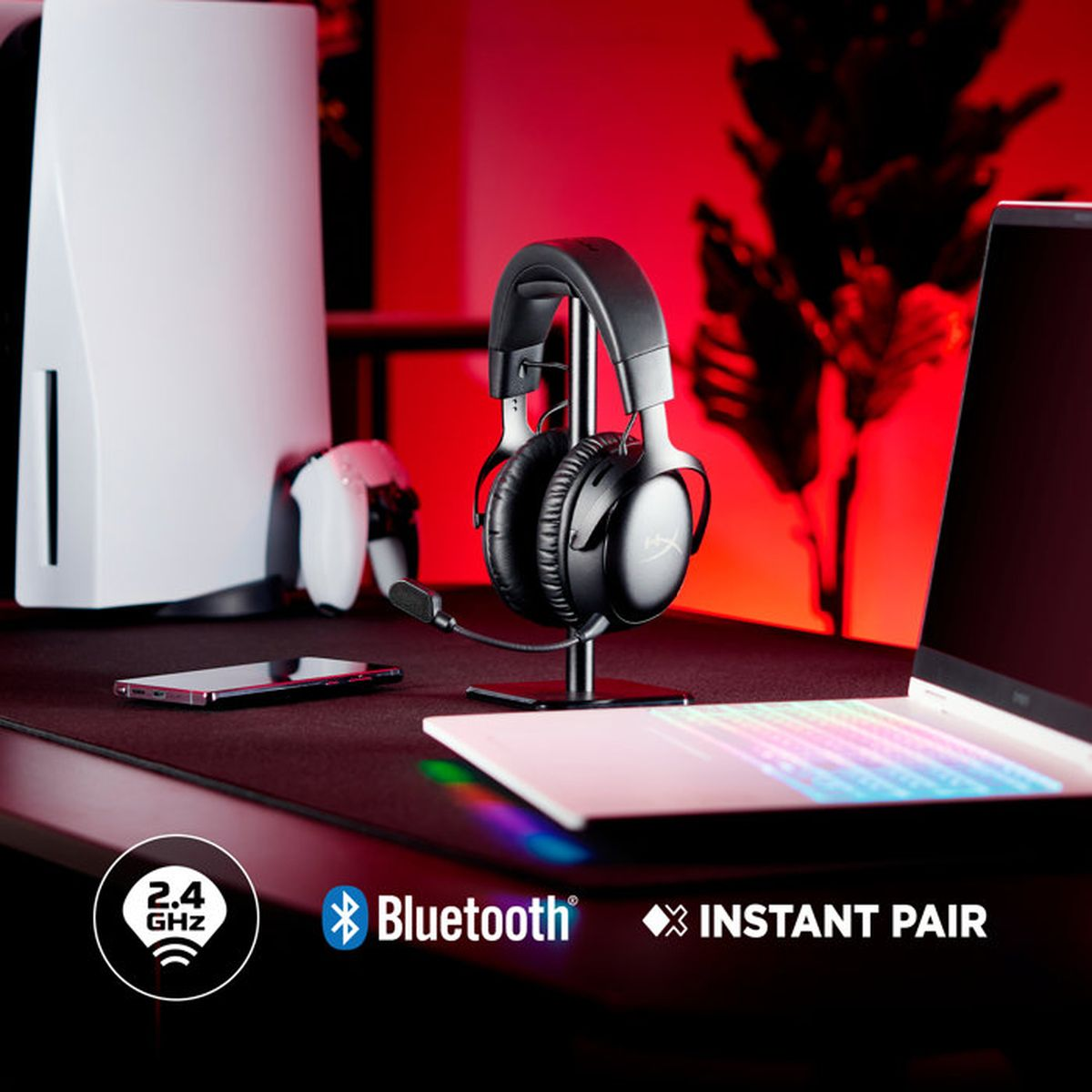 Cuffie da gioco nere su supporto su una scrivania con laptop e console su sfondo rosso.