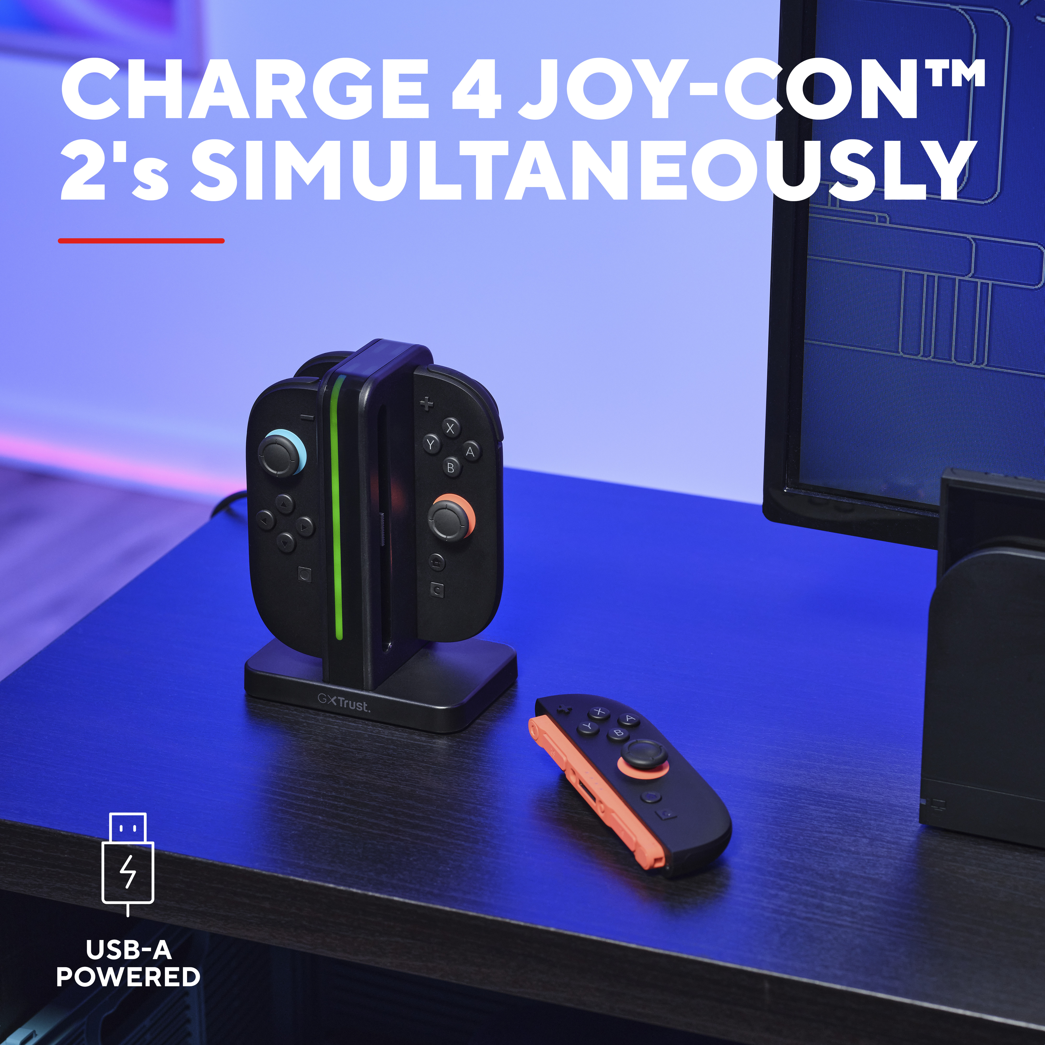 Eine Ladestation lädt zwei schwarze Joy-Cons auf einem blauen Schreibtisch auf.