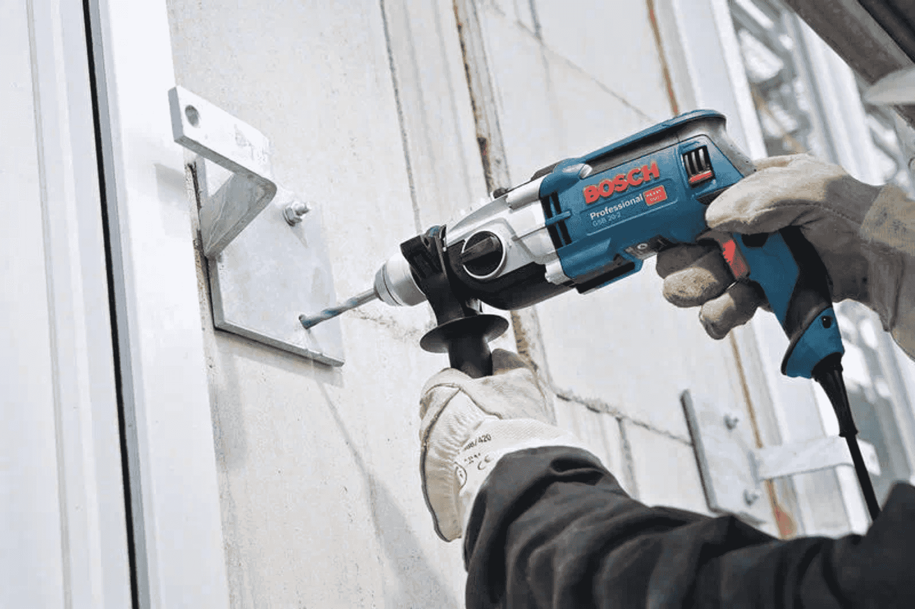 Un trabajador con guantes usa un rotomartillo azul de Bosch para perforar una pared.