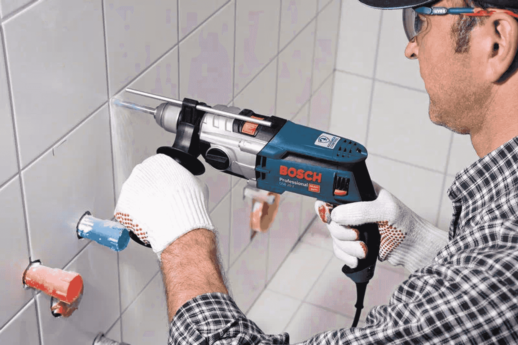 Un trabajador con gafas de seguridad usa un taladro azul Bosch en azulejos blancos.