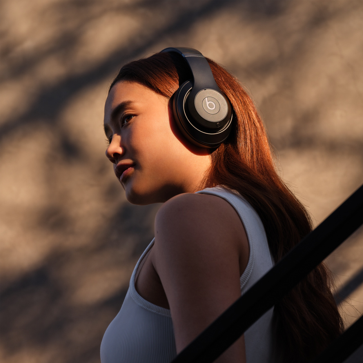Una giovane donna con i capelli rossi indossa cuffie nere e un top bianco alla luce calda del sole.