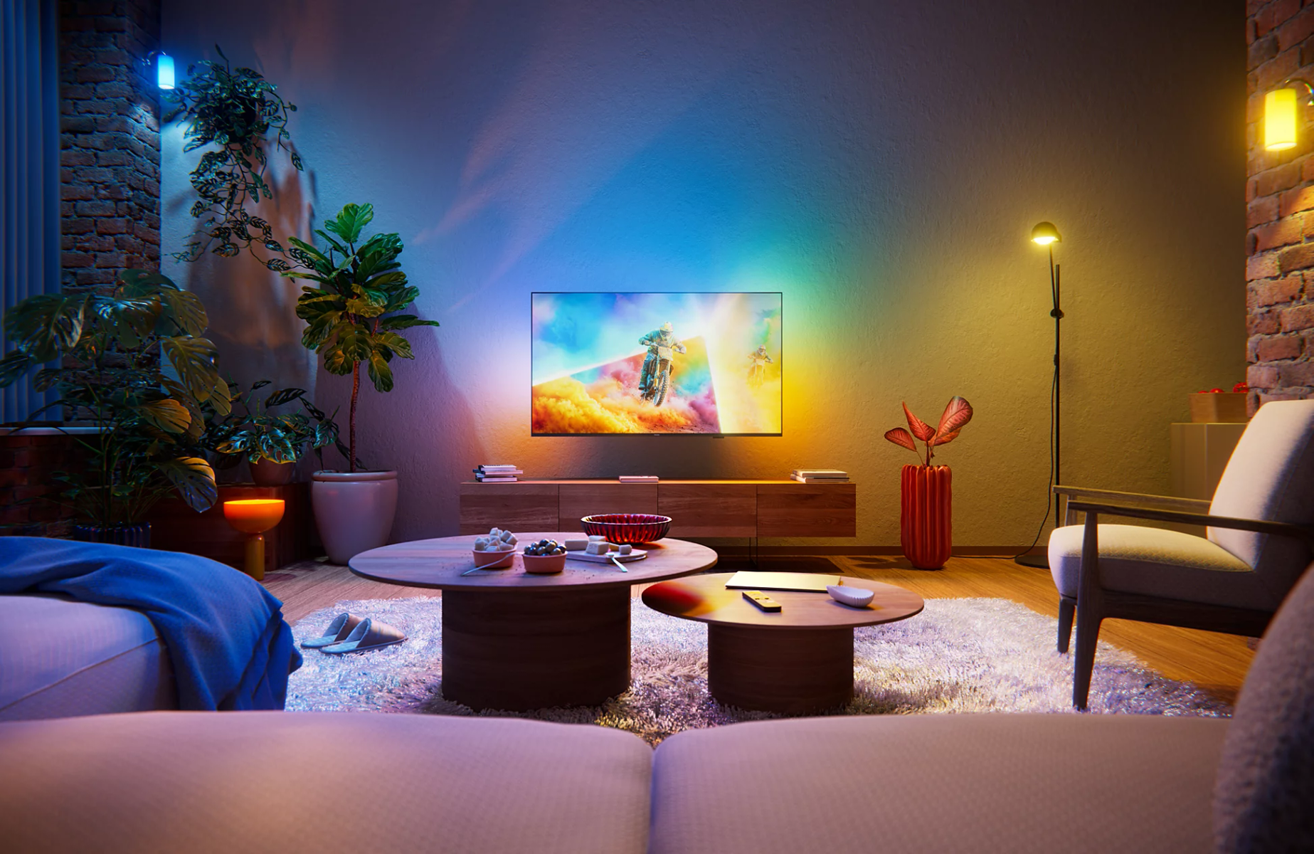 Sala con televisor iluminado, mesas de centro de madera, sofá, plantas y luz ambiental azul y amarilla.