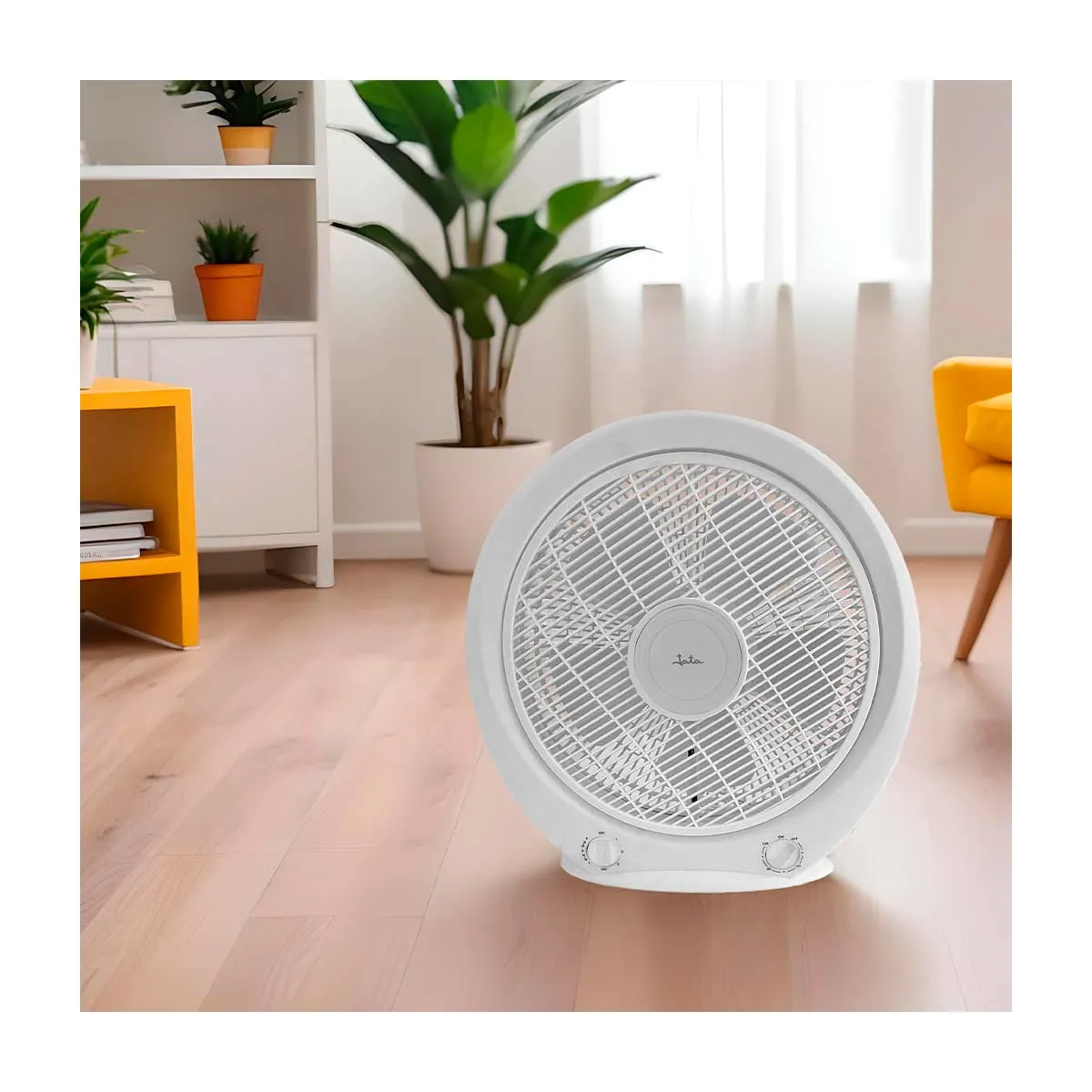 Ein weißer Bodenventilator steht auf einem Holzfußboden in einem hellen Zimmer mit Pflanzen und Möbeln.