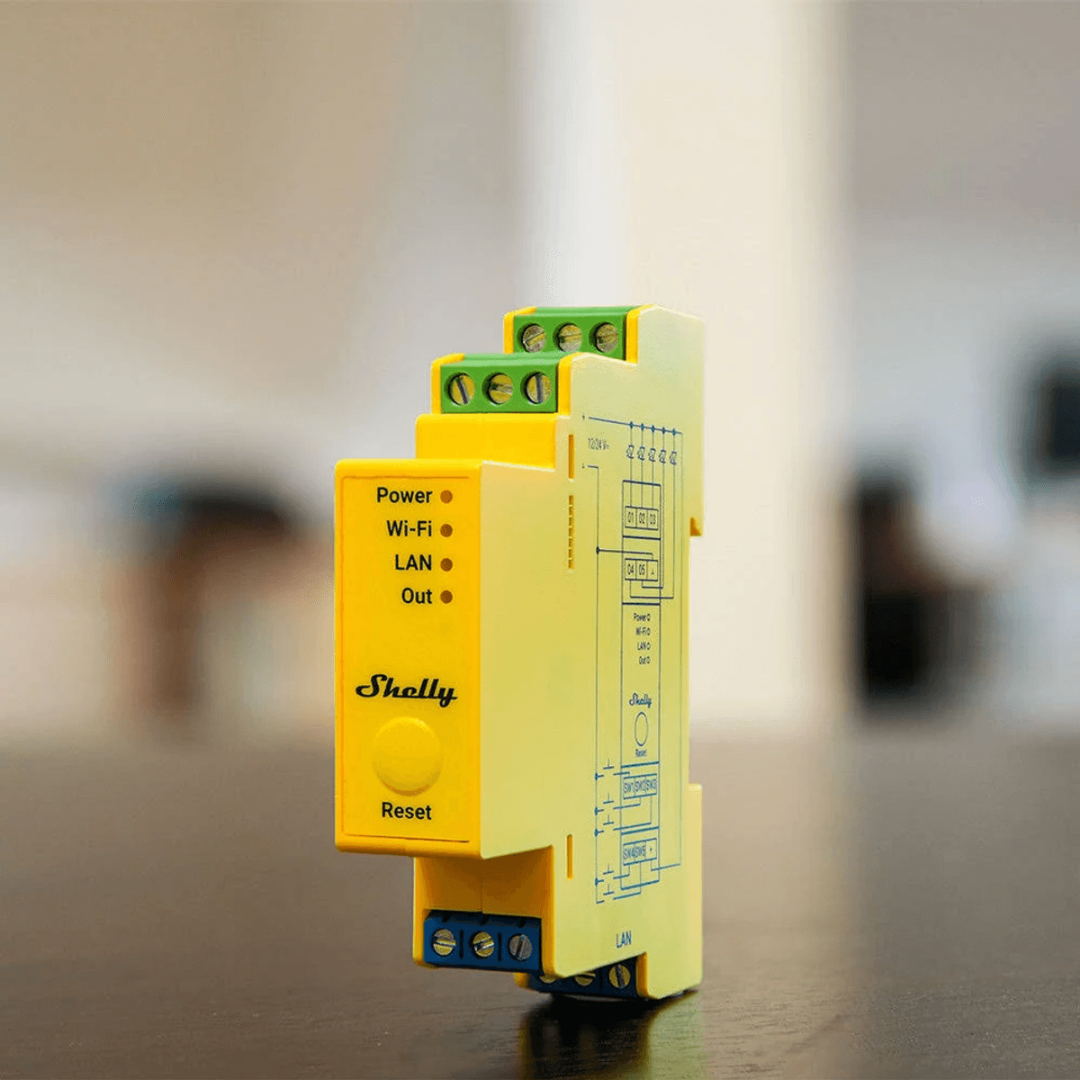 Módulo de relé Shelly amarillo en una mesa con LED de encendido, Wi-Fi, LAN y salida, y bloques de terminales verdes y azules.