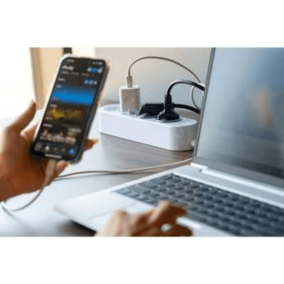Una persona usa una computadora portátil y sostiene un teléfono inteligente con una regleta de enchufes.