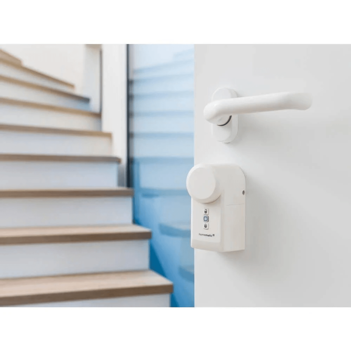 Ein weißes Homematic Smart Lock an einer weißen Innentür mit Griff, im Hintergrund eine Holztreppe.