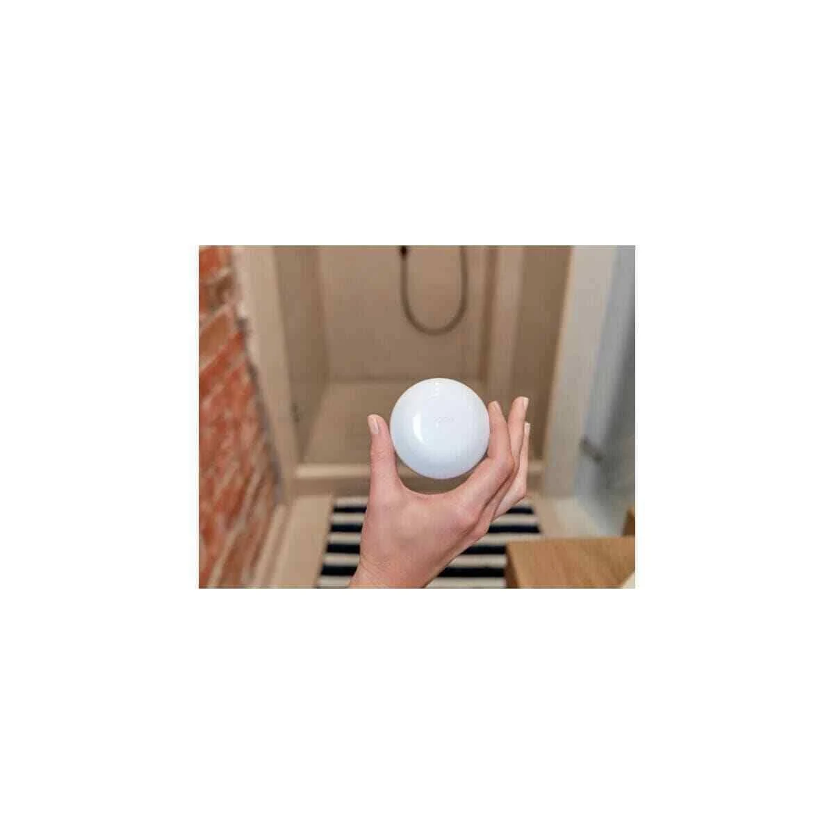 Una mano tiene una sfera bianca in una stanza con parete di mattoni e doccia.