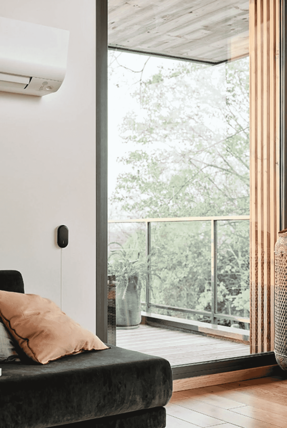 Sala de estar con cojines, aire acondicionado y dispositivo en la pared, con vista a un balcón verde.