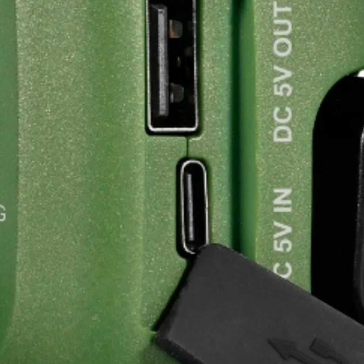 Zbliżenie zielonego urządzenia z portami USB oraz napisem DC 5V OUT i DC 5V IN z wtyczką.