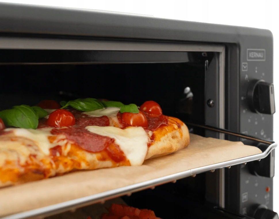 Pizza z roztopionym serem, salami, pomidorami i bazylią piecze się w czarnym mini piekarniku.