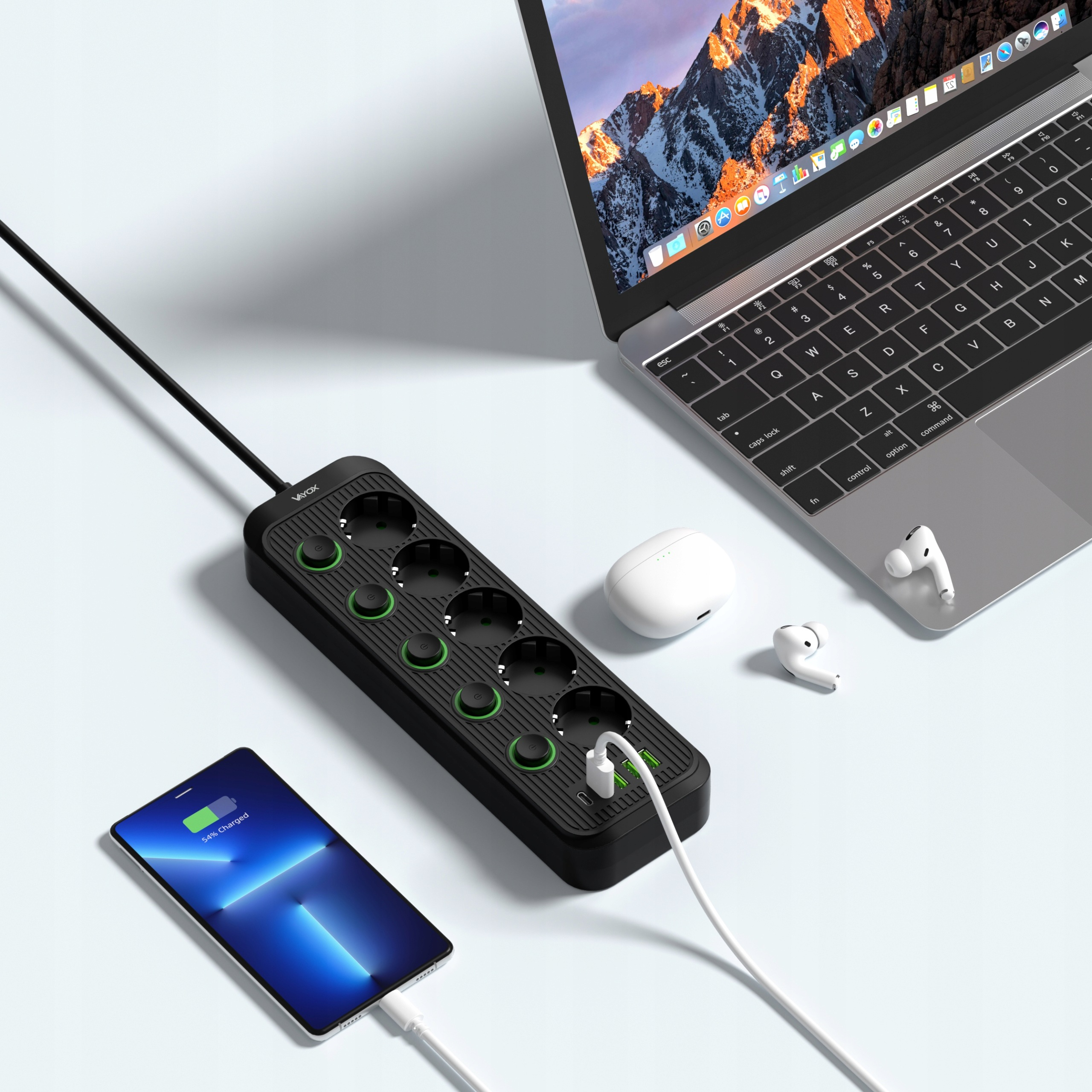 Czarna listwa zasilająca ładuje smartfon, obok laptopa i słuchawek na biurku.