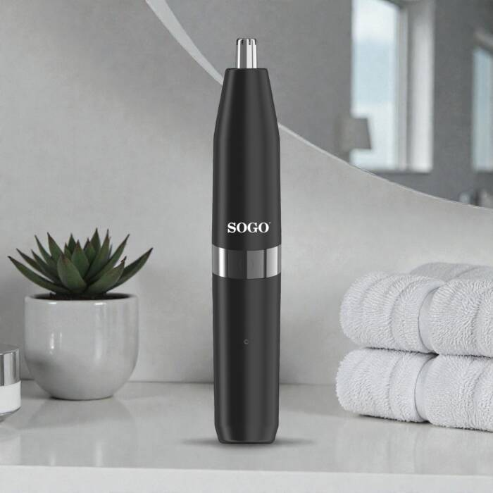 Un rifinitore per peli del naso SOGO nero si trova su un ripiano del bagno accanto a una pianta e asciugamani.
