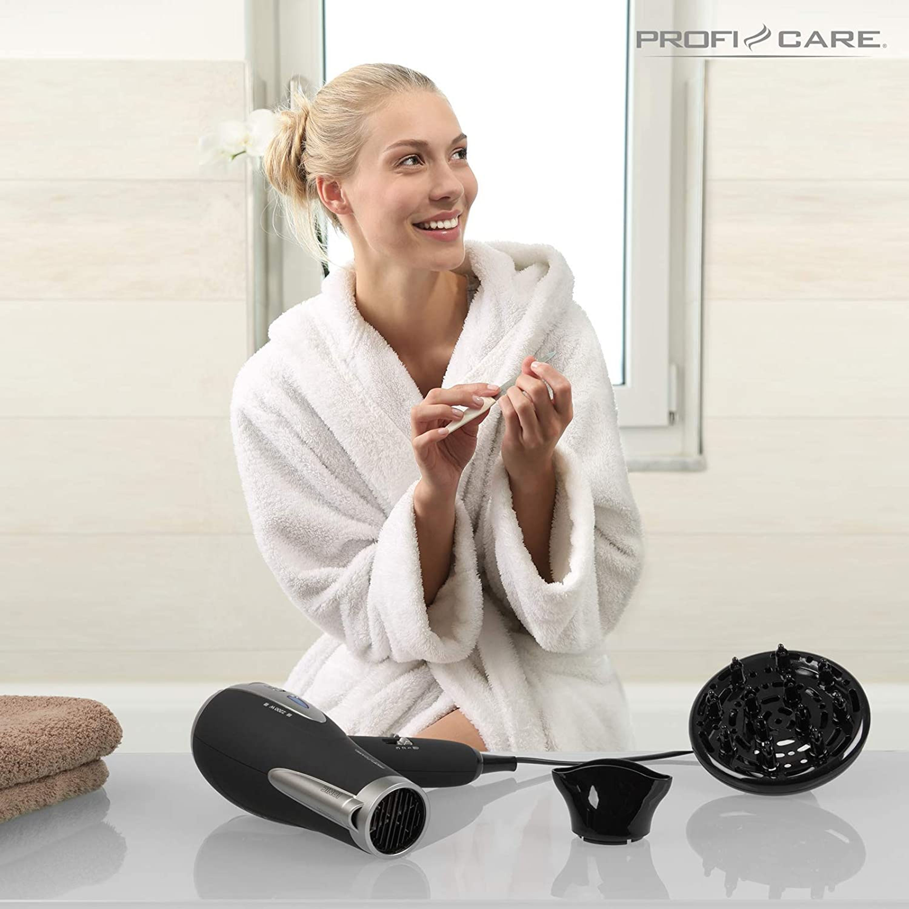 Une femme souriante en peignoir blanc se lime les ongles près d'un sèche-cheveux noir sur un comptoir.