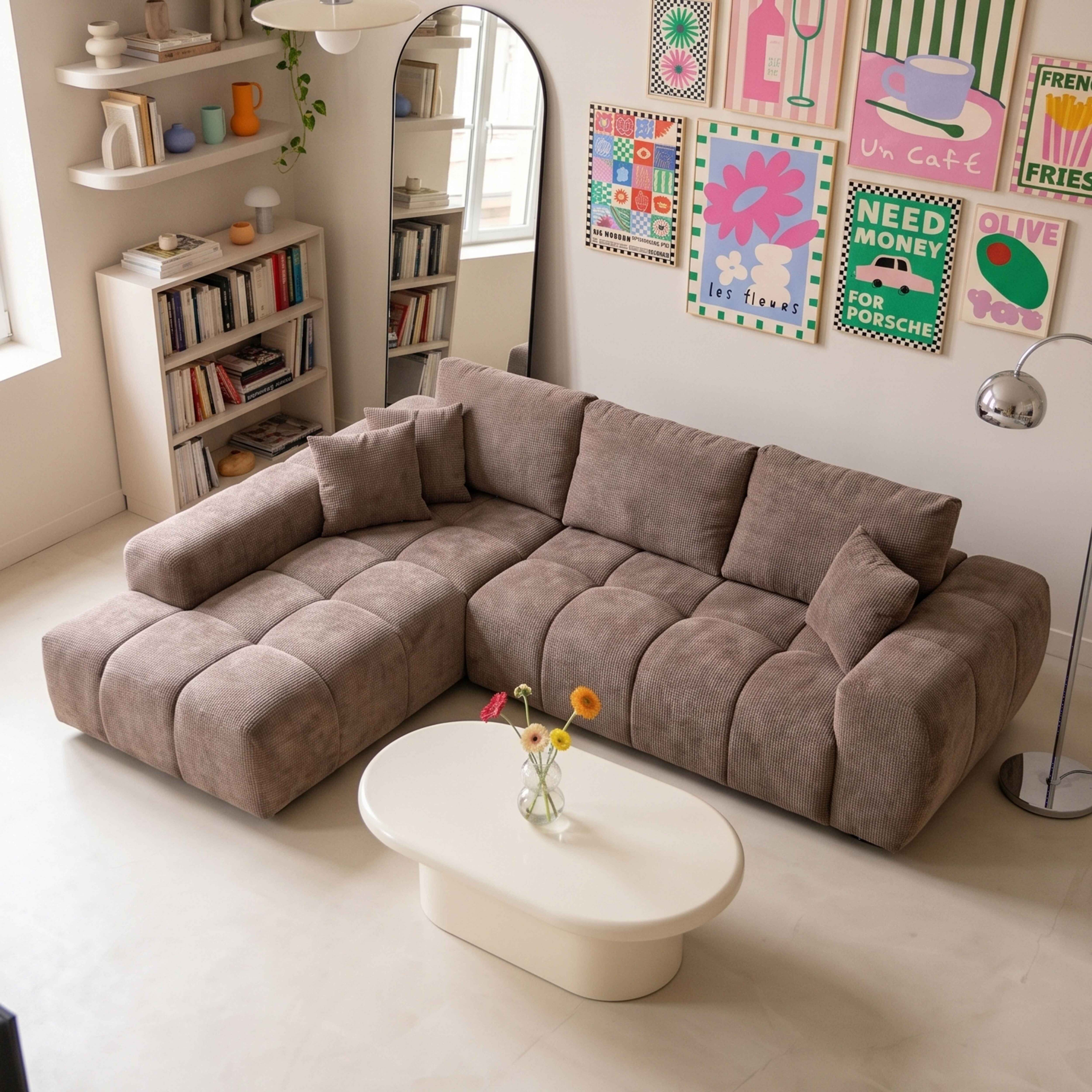 Ein beige Ecksofa steht in einem hellen Raum mit weißem Couchtisch, Bücherregalen und bunter Wandkunst.