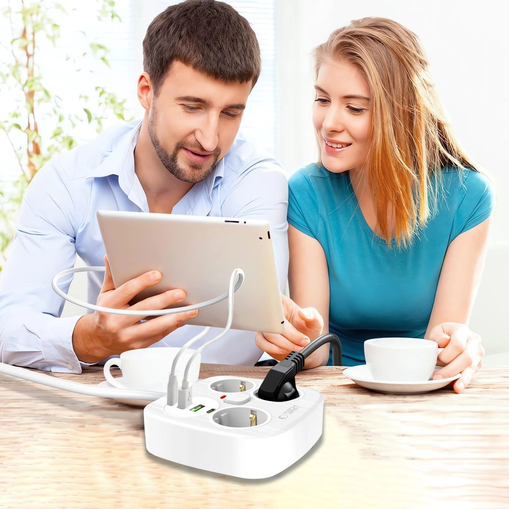 Ein Paar sitzt an einem Tisch mit Kaffeetassen und schaut auf ein Tablet, verbunden mit einer weißen Mehrfachsteckdose.