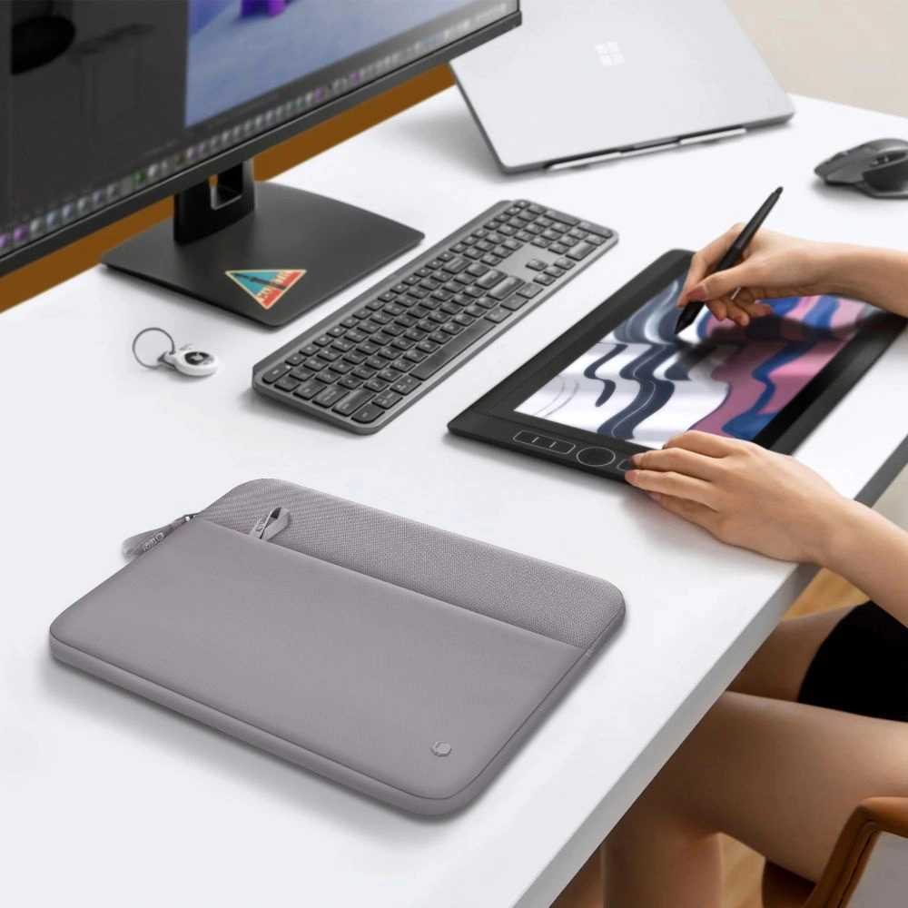 Une personne dessine sur une tablette graphique sur un bureau blanc avec un écran, un clavier et une housse grise.